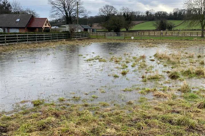 A flooded field with standing water in front of farm buildings